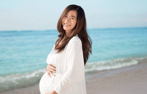 Mulher grávida abraça carinhosamente a barriga na praia: fique bem informada sobre sua saúde para uma gestação saudável