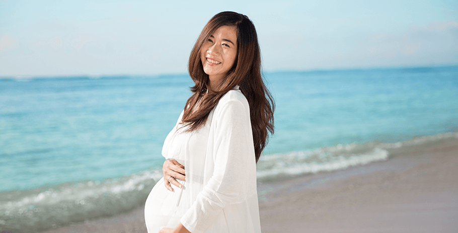 Mulher grávida abraça carinhosamente a barriga na praia: fique bem informada sobre sua saúde para uma gestação saudável