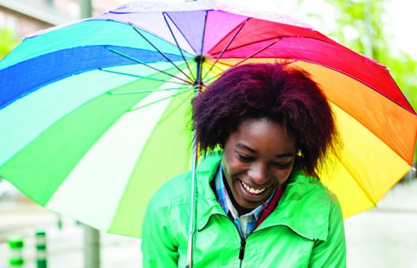 Mulher jovem com guarda-chuva colorido passeando na chuva.
