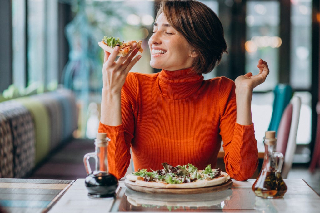 Mulher sentada em mesa de restaurante comendo uma refeição saudável