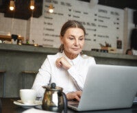 Mulher sentada em um café, pesquisando em um notebook sobre o que é menopausa