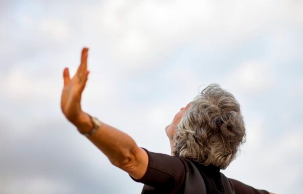 Mulher idosa de braços abertos olhando para o céu.