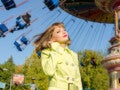 Mulher jovem vestindo casaco amarelo em frente a um carrossel em parque de diversões