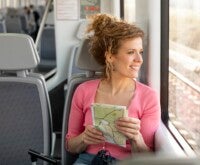 Mulher com mapa nas mãos sentada viajando de trem olha pela janela