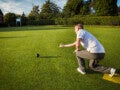 Homem de meia idade agachado em gramado fazendo lançamento de bola em jogo de bocha ou pétanque. Entender o que é colesterol é importante para cuidar melhor da saúde cardiovascular