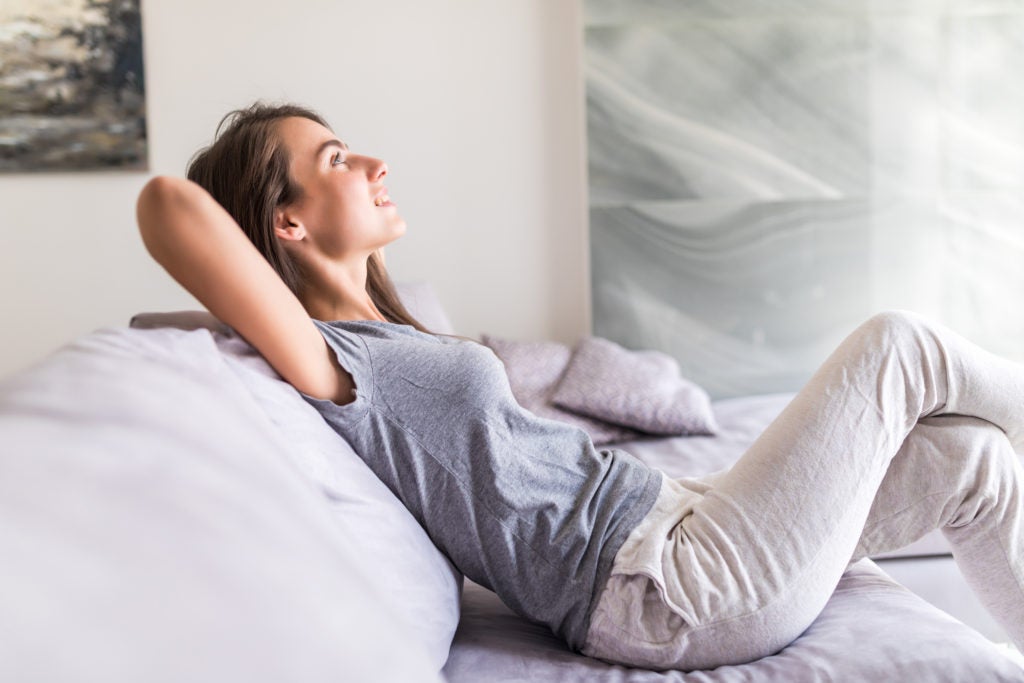 Mitos e verdades sobre a enxaqueca:  mulher jovem relaxa com as mãos atrás da cabeça sentada em sofá