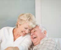 Casal de idosos dá risadas, sentados no sofá